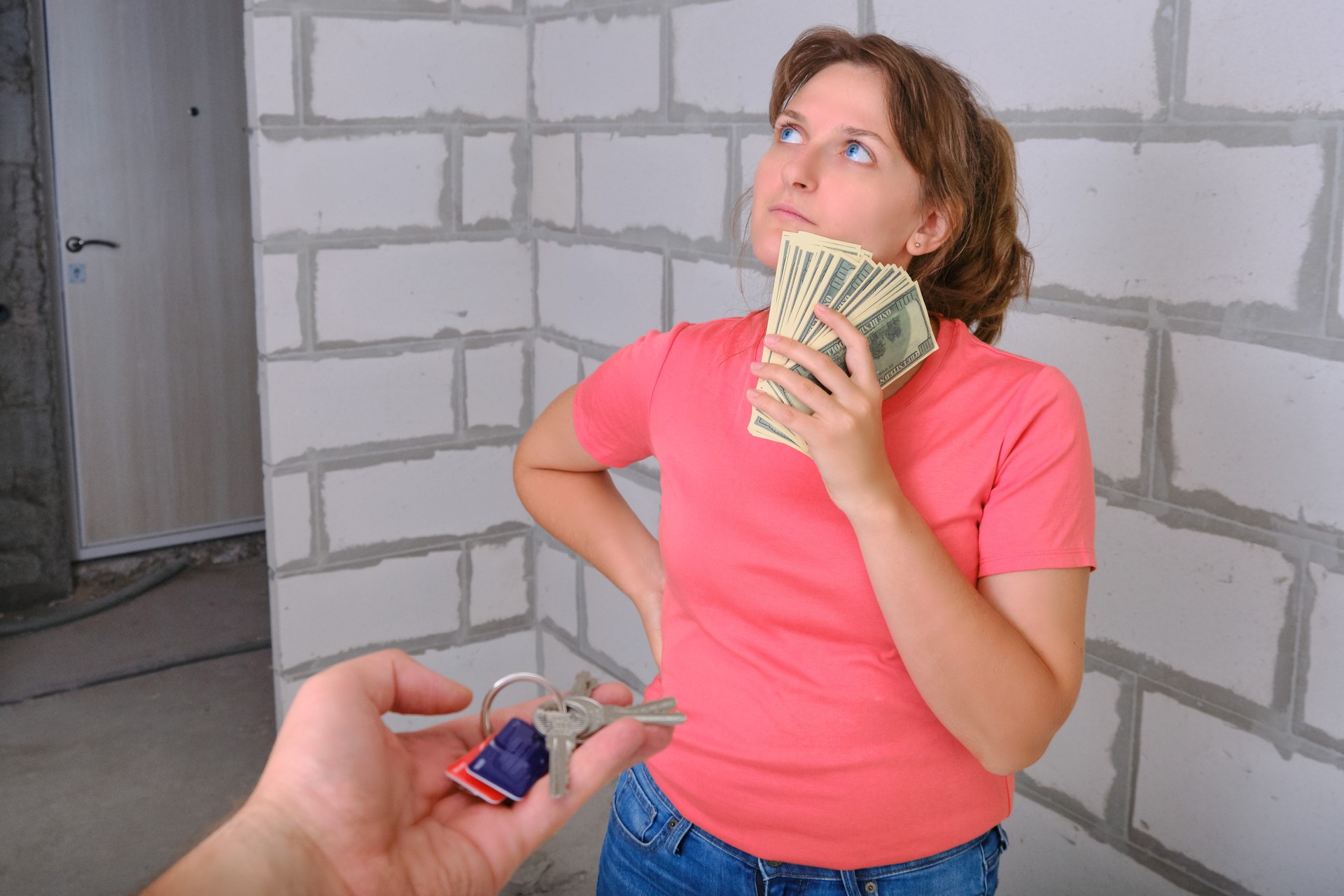 A young woman with us dollars in her hands thinking about buying a new apartment. The girl holds the money and hesitates to buy a built house.