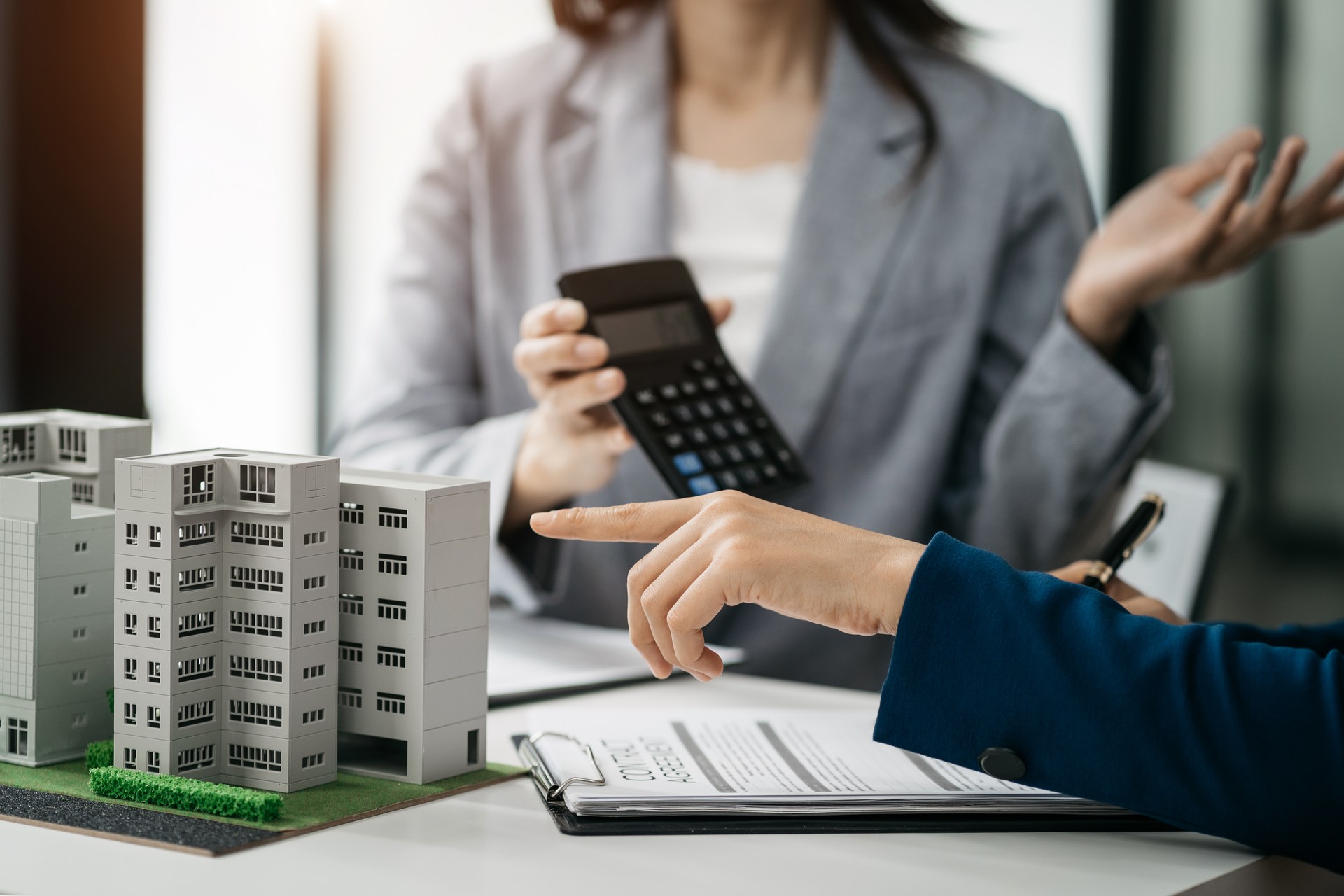 home loan officer uses a calculator with a house plan on a wooden table.